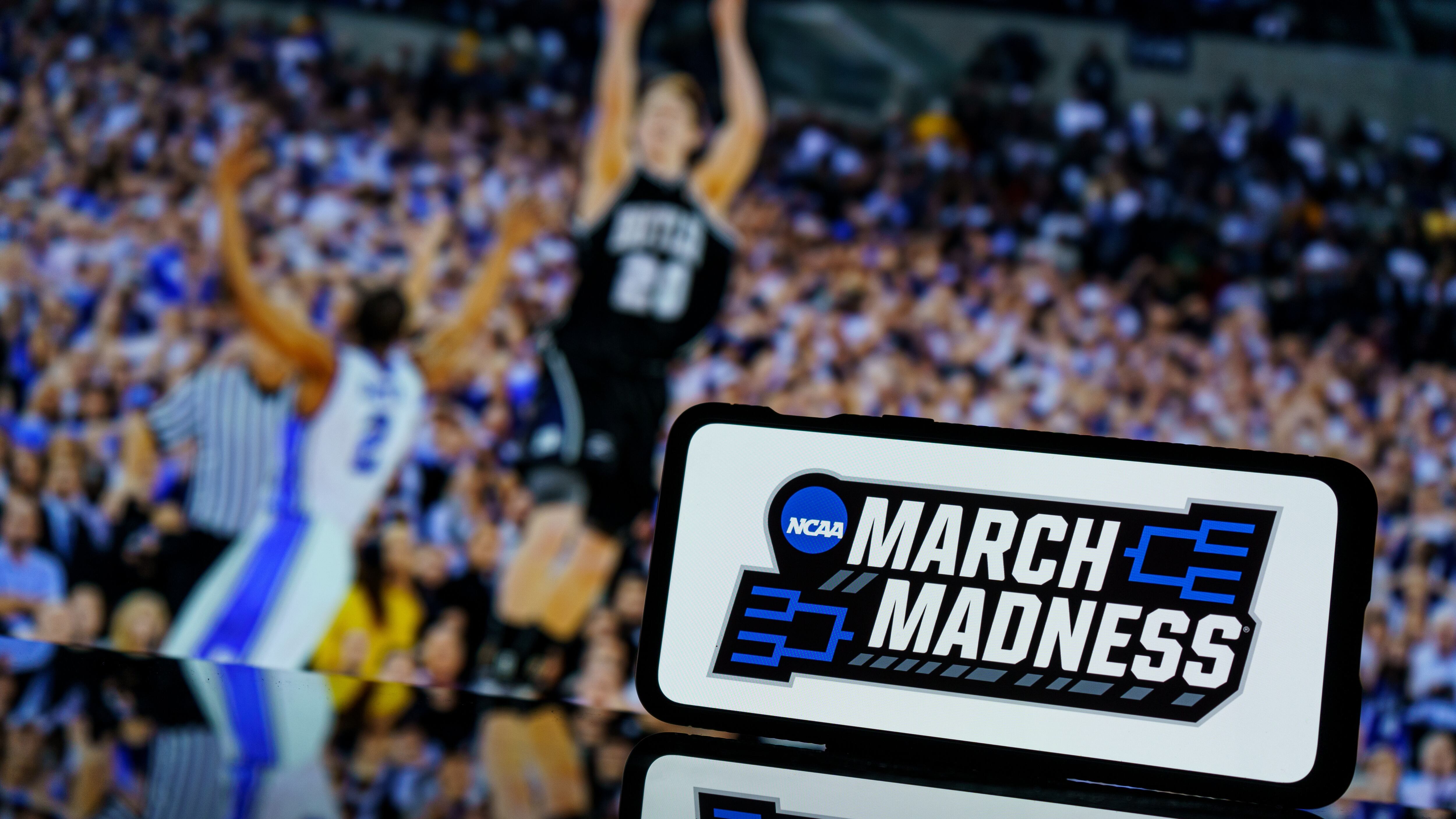 March madness logo on screen and NCAA basketball game play on TV in the background